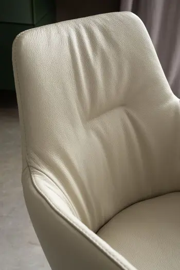 Rückenlehne eines beigen Polsterstuhls mit Lederbezug, der Stuhl hat eine Quernaht am Rücken und Armlehnen