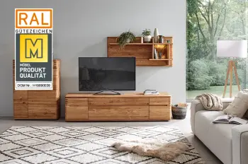 Gütesiegel "Goldene M" auf einem Bild einer Massivholz Wohnwand dekoriert mit vielen Pflanzen und beleuchtetem Regaleinsatz beim Highboard.