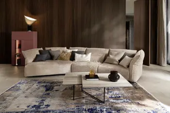 Moderner Couchtisch mit zwei Tischplatten und schwarzem Gestell vor einem beigen Sofa mit trapezförmiger Sitzfläche.