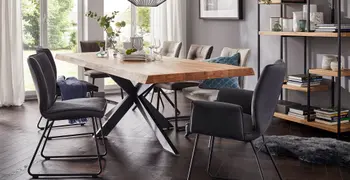 Esszimmerstühle aus dunkelm und hellem Grau mit und ohne Armlehne und mit Metallgestell um einen Esstisch mit Massivholztischplatte, auf dem Teller und Gläser sowei Vasen mit Blumen stehen.