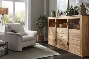 Beiger Sessel mit umgeklappter Kopflehne in einem gemütlichen Raum mit Stehlampe. mehreren Pflanzen und Massivholz Highboard.