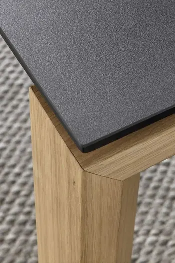 Ecke eines Esstisches mit Schwarzer Tischplatte und Massivholzgestell.