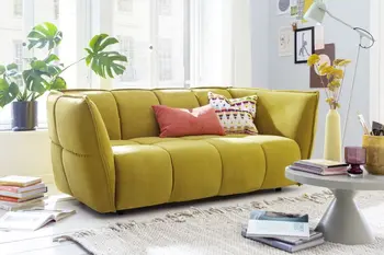 Modernes Sofa in Senfgelb in hellem Wohnzimmer mit rundem Beistelltisch. 