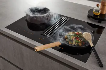 Kochfeld mit integriertem Dunstabzug auf dem zwei dampfenden Pfannen.