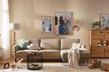 Beiges Leder Ecksofa mit schwarzen Kufen, auf der Sitzfläche liegen drei Kissen in grün und beige und eine beige Decke.