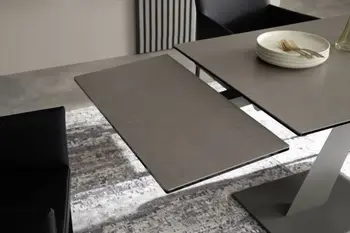 Moderner schwarzer Esstisch, bei dem die Verlängerungsplatte komplett unter dem Tisch herausgezogen wurde aber noch nicht am Tisch befestigt ist.