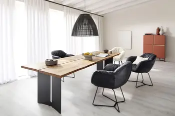 Ein weißer Teddy Stuhlsessel und drei schwarze Stuhlsessel mit dicker Polsterung und schwarzem Metallgestell um einen Massivholz Esstisch.