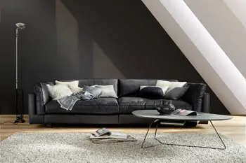 Modernes großes schwarzes Ledersofa mit hohen dick gepolsterten Armlehnen vor einer schwarzen Wand.