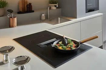 Kochfeld einer grauen Designküche, auf der eine Pfanne mit Gemüse steht.