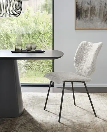 Moderner Esszimmerstuhl in weißem Bouclé-Stoff neben schwarzem Esstisch.