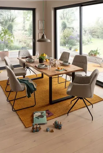 Moderner Massivholz Esstisch mit schwarzen Kufen in einem hellen Raum, um den Tisch stehen mehrere graue Stühle mit und ohne Armlehne