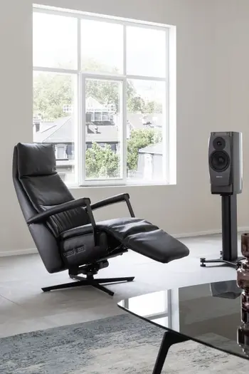 Schwarzer Relaxsessel mit Lederbezug mit ausgefahrener Fußlehne vor einem großen Fenster mit weißen Sprossen.