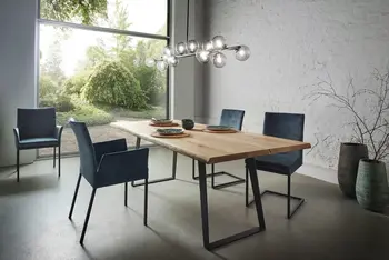 Moderner Massivholz Esstisch mit schwarzen Kufen, um den mehrere petrolfarbene Stühle stehen.