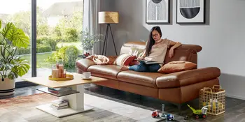 Frau sitzend auf rotbraunem Ledersofa vor quadratischem Couchtisch.