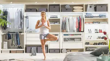 Großer offener Kleiderschrank ohne Türen mit Kleiderstange, Regalfächer, Schuhablage, Hosenauszug befüllt mit Kleidung und Schuhen und Aufbewahrungsboxen, davor steht eine Frau und macht eine Yoga-Pose.