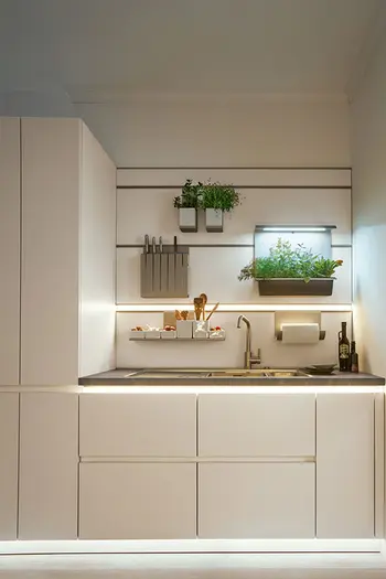 Weiße Küchenzeile mit Beleuchtung an der Nischenrückwand und unterhalb der Leisten.