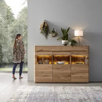 Sideboard aus Massivholz mit beleuchteten Regalböden die dekoriert sind mit Vasen und Tellern und Pflanzen auf dem Sideboard.