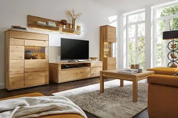 Massivholz Wohnwand mit Glaselementen bestehend aus TV-Lowboard, Vitrine, Highboard und hängendem Wandregal in einem gemütlichen Wohznzimmer.