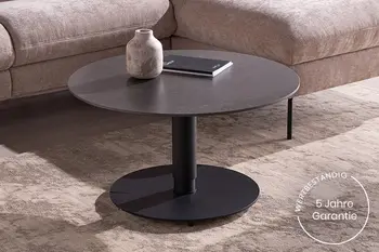 Runder Couchtisch mit schwarzer Keramikplatte und schwarzem Fuß vor beigem Sofa.