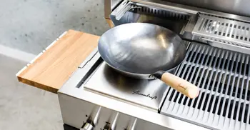 Wokpfanne auf der Kochflaeche einer Flammkraft-Outdoorkueche. 