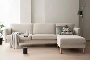 Beiges Stressless Copenhagen Sofa mit Holzfüßen in einem modernen Wohnzimmer, dekoriert mit grauen und gemusterten Kissen. Ein schwarzer Beistelltisch mit einer Karaffe und Glas steht daneben.