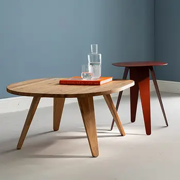 Couchtisch aus Holz im Skandi-Look neben rotem Beistelltisch aus Metall vor hellblauer Wand.