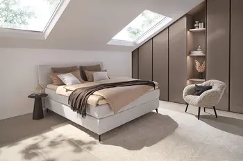 Graues Designer Boxspringbett gemütlich dekoriert in einem hellen Zimmer.