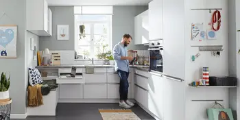 Mann in kompakter Kueche in U-Form mit weissen Kuechenfronten und Granitarbeitsplatte.