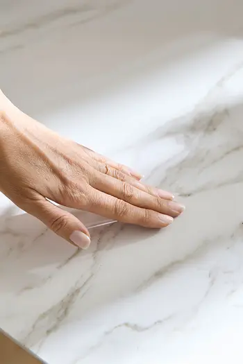 Detailbild von Keramiktischplatte in Marmoroptik, Frau streicht mit Hand über Oberfläche.