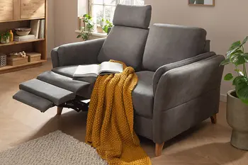 Graues Sofa mit ausgeklappter Relaxfunktion zum Entspannen, dekoriert mit senffarbener Decke.