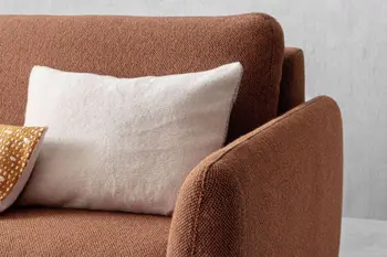 Moderne Armlehne eines rostroten Sofas, auf dem Kissen liegen.