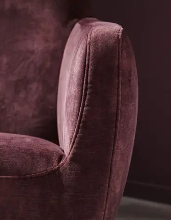 Armlehne eines Sessels, der mit Stoff in Beere bezogen ist.