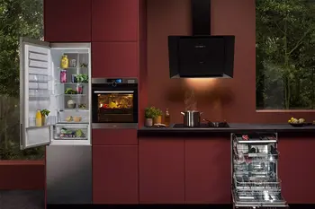 Rote Designküche mit geöffneter Kühlgefrierkombination und Geschirrspüler, sowie beleuchtetem Backofen.