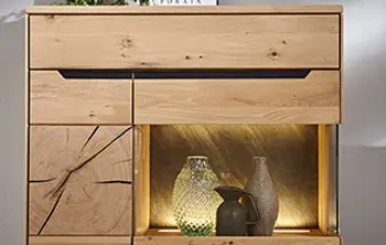 Detailansicht einer hochwertigen Holzkommode mit integrierter LED-Beleuchtung – modernes Massivholzdesign mit sichtbarer Baumkante und dekorativer Glasvase im beleuchteten Fach. Ideal als stilvolles Stauraummöbel im Wohnzimmer.