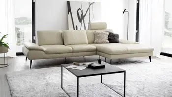 Beiges Ledersofa, bei dem eine Kopfstütze hochgeklappt ist in einem hellen Raum mit großen Fenstern.