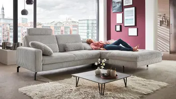 Frau liegt auf hellgrauem Stoffsofa mit Relaxfunktion in Wohnzimmer.