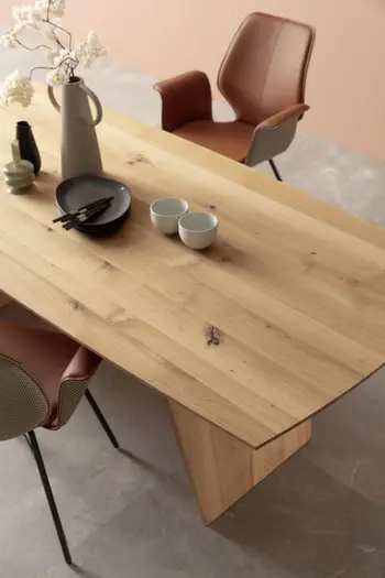 Moderner Esstisch aus Massivholz mit Tischplatte in organischer Form, auf der eine Karaffe, Tassen, Teller und Besteck liegen.