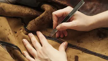 Hand schneidet Leder mit einem Cutter-Messer.