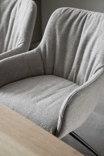 Beiger Armlehnstuhl, der einen Stoffbezug hat und am Rücken eine moderne Faltenbildung.