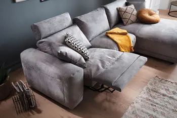 Graues Ecksofa mit Stoffbezug, bei dem die Relaxfunktion auf der linken Seite ausgefahren ist, dekoriert mit mehreren Kissen in beige, grau, weiß und gelb.
