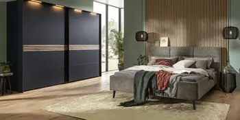 Schlafzimmer mit Polsterbett, Schwebetürenschrank und Holzlamellenwand.