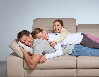 Vater mit zwei lachenden Kindern auf einem beigen Ledersofa – fröhlicher Familienmoment auf einer gemütlichen Couch mit verstellbarer Rückenlehne