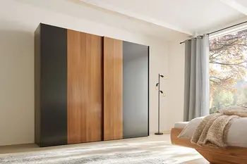 Großer Schwebetürenschrank aus Massivholz mit schwarzen Akzenten in einem hellen gemütlichen Schlafzimmer eines Bauernhauses.