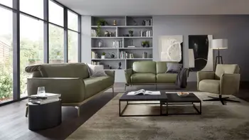 Olivegrünes Ledersofa mit umgeklappten Kopfstützen und silbernen Beinen neben einem weiteren grünen Ledersofa und einem grünen Ledersessel in einem hellen modernen Raum mit großen Fenstern.