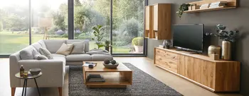 Hellgraues Stoffsofa in gemuetlichem Wohnzimmer mit Massivholz-Wohnwand und -couchtisch.