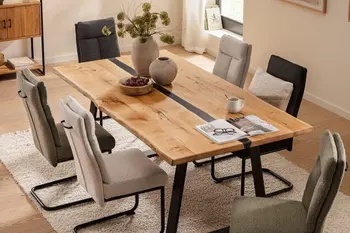 Esstisch mit Massivholzplatte und schwarzem Metallgestell mit einem schwarzen Element in der Tischplatte, um den Tisch herum Freischwinger in grau, beige und olivegrün.