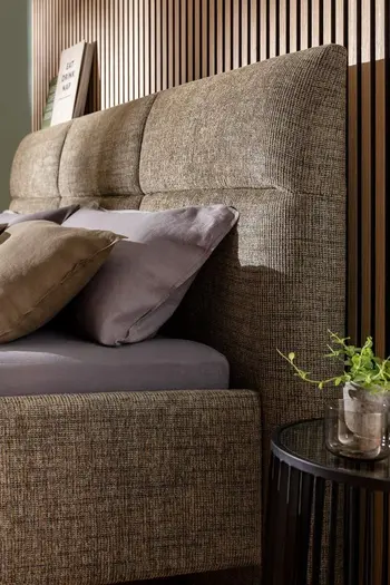 Kopfteil eines moosgrünen Polsterbettes, das Absteppungen hat.