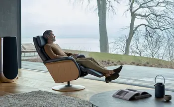 Stilvoller Stressless Relaxsessel in einem modernen Wohnzimmer mit Blick auf eine idyllische Landschaft und große Fensterfronten, die viel Tageslicht hereinlassen.