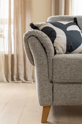 Abgerundete Armlehne eines grauen Ecksofas mit Holzbeinen.