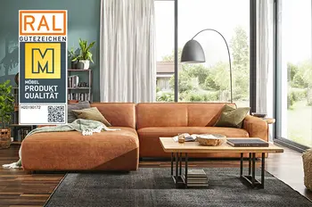 Gütesiegel "Goldene M" auf einem Bild von einem Ecksofa mit Lederbezug in Cognac in einem hellen Wohnzimmer mit dunklem Teppich und Holzboden.